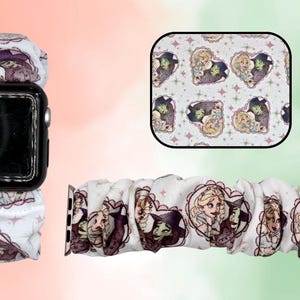 May include: White Apple Watch band with a repeating pattern of cartoon characters in heart-shaped frames. The band features a witch and a princess. The watch band is shown attached to a black Apple Watch.
