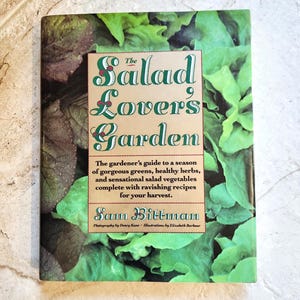 May include: The Salad Lover's Garden book cover features a close-up of lush green lettuce leaves with the title in a stylized font. The book is a guide to growing salad greens, herbs, and vegetables.