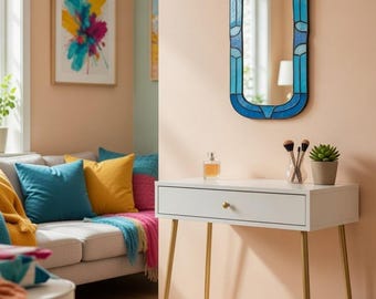 Könnte beinhalten: Ein weißer Schminktisch mit goldenen Beinen und einer Schublade, gekrönt von einem blau gerahmten Spiegel. Der Spiegel hat ein Buntglasdesign. Eine kleine Sukkulente und Make-up-Pinsel stehen auf dem Tisch. Ein Gemälde und ein Sofa mit bunten Kissen befinden sich im Hintergrund.