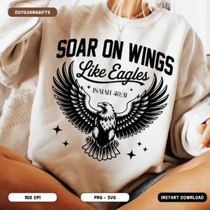 Könnte beinhalten: Cremefarbenes Sweatshirt mit einem schwarzen Adler-Grafik und dem Text "SOAR ON WINGS Like Eagles" mit "ISAIAH 40:31" darunter. Das Design enthält vier kleine Sternformen. Das Sweatshirt ist eine PNG- und SVG-Datei.