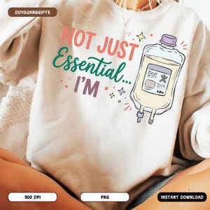 May include: White sweatshirt with the text "NOT JUST Essential... I'M" in pink, teal, and purple. A cartoon illustration of an IV bag is on the right. The sweatshirt is a casual style.