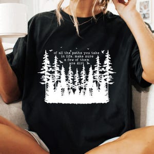 Puede incluir: Camiseta negra con un gr&aacute;fico blanco de un bosque y el texto "of all the paths you take in life, make sure a few of them are dirt".