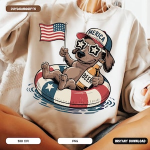 Könnte beinhalten: Weißes Sweatshirt mit einem Cartoon-Hund, der eine sternförmige Sonnenbrille und einen Hut mit der Aufschrift "America" trägt. Der Hund schwimmt auf einem rot-weiß-blauen Schwimmring und hält ein Bier und eine amerikanische Flagge.