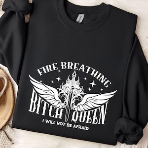 Pode incluir: Camisola de moletom preta com um design gr&aacute;fico branco que apresenta uma espada com asas e o texto "Fire Breathing Bitch Queen I Will Not Be Afraid."