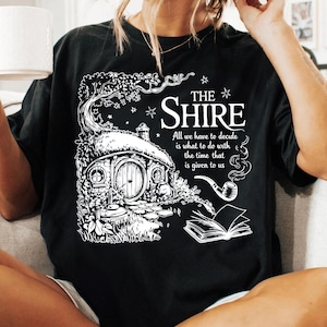 May include: Black t-shirt with a white graphic of a hobbit house, a pipe, and a book. The text reads "THE SHIRE All we have to decide is what to do with the time that is given to us."
