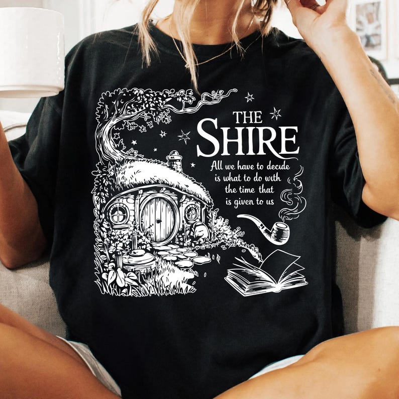 May include: Black t-shirt with a white graphic of a hobbit house, a pipe, and a book. The text reads "THE SHIRE All we have to decide is what to do with the time that is given to us."