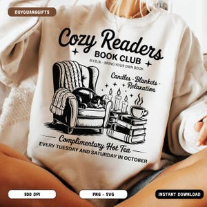Könnte beinhalten: Weißes Sweatshirt mit schwarzem Grafikdesign. Das Design zeigt eine gemütliche Leseszene mit einer Katze in einem Stuhl, Kerzen, Büchern und dem Text "Cozy Readers Book Club". Enthält den Text "Complimentary Hot Tea".