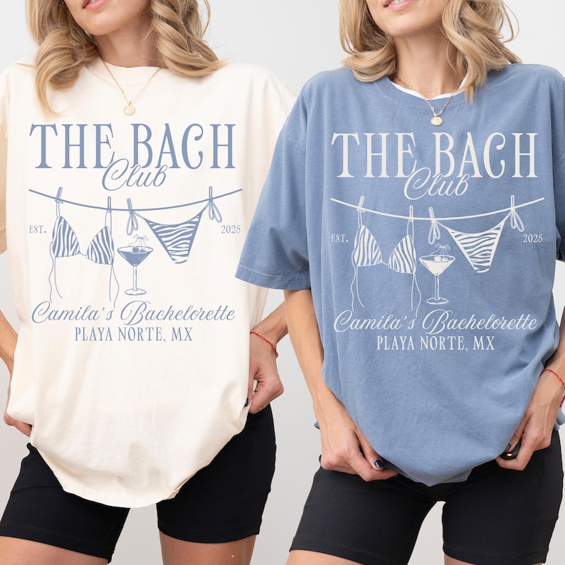 May include: Two t-shirts, one cream and one blue, with the text "THE BACH Club" and a bikini and cocktail graphic. The text "Camila's Bachelorette PLAYA NORTE, MX" is also printed on the shirts. The shirts are short-sleeved.