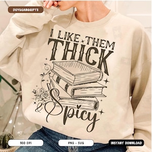 May include: A beige sweatshirt with a graphic design that says "I like them thick & spicy" with a stack of books and floral accents.