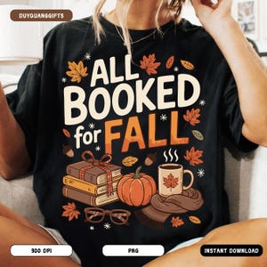 May include: Black t-shirt featuring the text "ALL BOOKED for FALL" in white and orange. The design incorporates autumn elements like leaves, a pumpkin, books, a coffee mug, and spectacles.