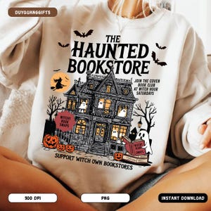 May include: A white sweatshirt featuring a graphic of a haunted house with ghosts, pumpkins, and bats. The text reads "THE HAUNTED BOOKSTORE" with additional text promoting a book club. The design includes the words "Witchy Book Swaps" and "Support Witch Own Bookstores".