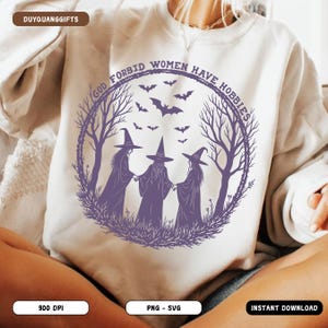 May include: A white sweatshirt with a purple graphic featuring three witches in hats, surrounded by a circular frame with the text "GOD FORBID WOMEN HAVE HOBBIES" and bats. The design is a digital download.