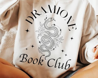 May include: Cream-colored sweatshirt with a black graphic design. The design features the words "Dramione Book Club" with a snake and floral illustration. The sweatshirt has a crew neck and long sleeves.