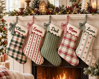 Op de afbeelding: Vijf stoffen kerstsokken hangen aan een witte schoorsteenmantel. Elke sok heeft een schulprand met een naam geborduurd in rood of groen: Oliver, Emma, Dad, Mom en Luna. De sokken hebben diverse patronen zoals ruiten, strepen en kleine strikjes, elk versierd met een groen-witte vichy-strik.