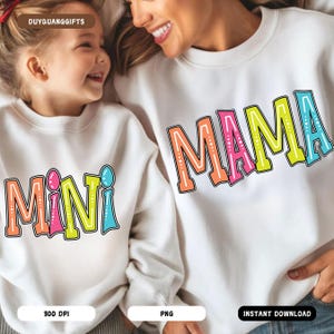 Puede incluir: Una sudadera blanca con la palabra "MAMA" en letras de colores con contorno blanco y lunares blancos. Una segunda sudadera blanca con la palabra "MINI" en letras de colores con contorno blanco y lunares blancos.