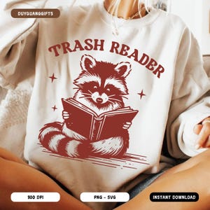May include: A white sweatshirt with a red raccoon reading a book. The text "Trash Reader" is printed in red above the raccoon.