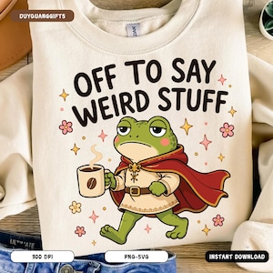 May include: Cream-colored sweatshirt with the text "OFF TO SAY WEIRD STUFF" and a cartoon frog wearing a cape and holding a coffee cup. The design includes pink flowers and stars.