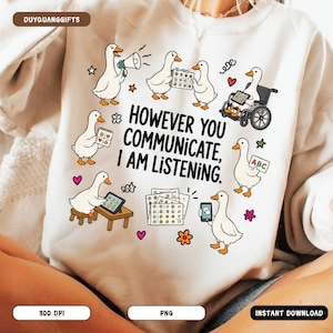 Puede incluir: Una sudadera beige con un gráfico de varios patos blancos usando diversas herramientas de comunicación. El texto dice: "HOWEVER YOU COMMUNICATE, I AM LISTENING." Los patos aparecen con objetos como un megáfono, una silla de ruedas, una tableta y tableros de comunicación, rodeados de pequeñas estrellas, corazones y flores de colores.
