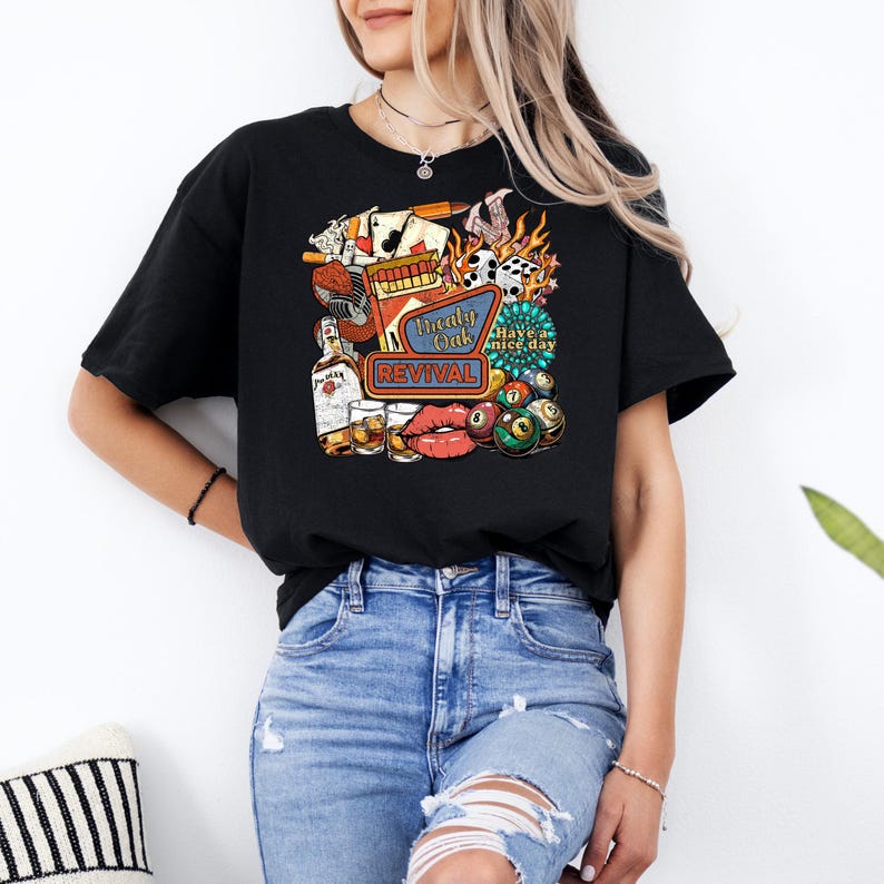 K&ouml;nnte beinhalten: Schwarzes T-Shirt mit einem farbenfrohen Grafikdesign. Das Design zeigt eine Whiskeyflasche, Spielkarten, W&uuml;rfel, eine Billardkugel und die Worte "Treaty Oak Revival" und "Have a nice day". Das T-Shirt wird mit einer blauen Jeans getragen.