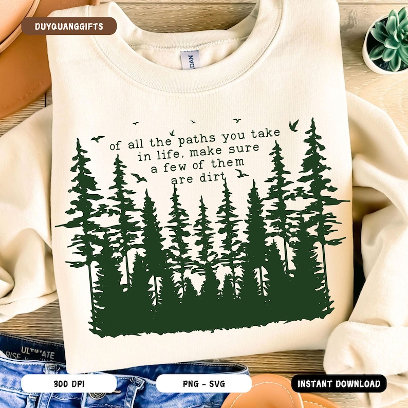 Puede incluir: Una sudadera de color crema con una silueta de bosque verde y el texto "of all the paths you take in life, make sure a few of them are dirt".