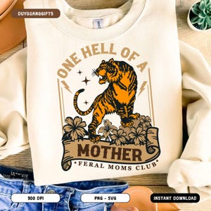 May include: A beige sweatshirt with a graphic design of a tiger with the text "One Hell of a Mother *Feral Moms Club*" printed on it.