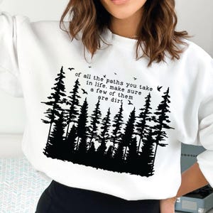 Puede incluir: Sudadera blanca con una silueta negra de un bosque y el texto "of all the paths you take in life, make sure a few of them are dirt".