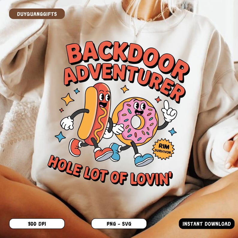 May include: Cream-colored sweatshirt with a cartoon graphic of a hot dog and donut. The text reads "BACKDOOR ADVENTURER" and "HOLE LOT OF LOVIN'". The hot dog and donut are smiling and wearing shoes. The graphic includes stars and the words "RIM SURVIVOR".