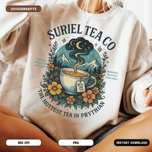 Könnte beinhalten: Weißes Sweatshirt mit farbenfrohem Grafikdesign für "Suriel Tea Co." Das Design zeigt eine Teetasse mit Dampf, der zu einem Halbmond aufsteigt, umgeben von Blumen und Bergen. Der Text enthält "Spill the Tea" und "The Hottest Tea in Prythian."