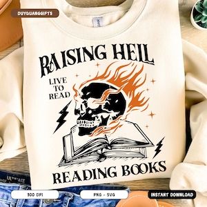 Könnte beinhalten: Cremefarbenes Sweatshirt mit einem schwarzen Totenkopf-Motiv, das von orangefarbenen Flammen umgeben ist, über einem offenen Buch. Der Text lautet "RAISING HELL LIVE TO READ READING BOOKS" mit Blitz- und Sternakzenten. Ein lässiges Sweatshirt.