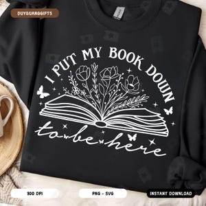 Könnte beinhalten: Schwarzes Sweatshirt mit weißem Text, der "Ich habe mein Buch abgelegt, um hier zu sein" lautet, mit einer weißen Umrandung eines offenen Buches mit Blumen und Schmetterlingen.