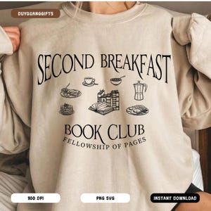 May include: A beige sweatshirt with the text "Second Breakfast Book Club Fellowship of Pages" in black. The design includes illustrations of books, coffee, and breakfast foods.
