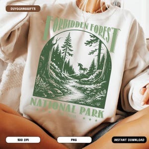 May include: A white sweatshirt with a green graphic design of a forest with a unicorn. The text "Forbidden Forest National Park" is printed on the sweatshirt.