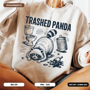 May include: Cream-coloured sweatshirt featuring a raccoon, toilet, and bin graphic. The text "Trashed Panda" is above the raccoon. A spilled bottle is on the ground. The sweatshirt is a casual, comfortable style.
