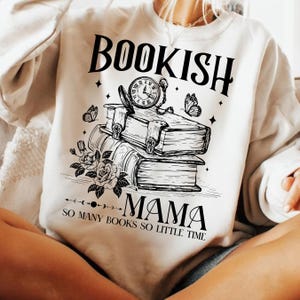 May include: White sweatshirt with a black graphic design of a stack of books, a clock, and butterflies. The text "Bookish Mama So Many Books So Little Time" is printed on the sweatshirt.