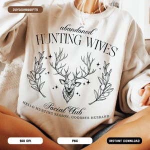 May include: A white sweatshirt with a black graphic design featuring a deer head with antlers, surrounded by leaves and stars. The text "abandoned hunting wives" and "Social Club" are also included in the design.