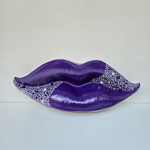 May include: Purple ceramic lips with a sparkly design. The lips are decorated with rhinestones and glitter.