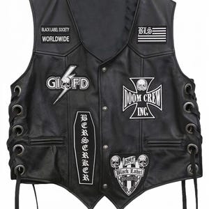 Puede incluir: Un chaleco de cuero negro con cordones laterales y ojales metálicos, decorado con varios parches bordados en blanco. Los parches incluyen los textos Black Label Society Worldwide, BLS, GIOFD, Doom Crew Inc, Berserker y Black Label Society.