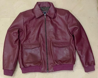 May include: A burgundy leather jacket with a collared neckline, a black zipper, and two front pockets. The jacket has a ribbed hem and cuffs. The jacket is a deep shade of red.