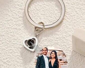 May include: A silver keychain with a heart-shaped charm that has a photo of a couple inside. The photo is of a man and a woman in formal attire.