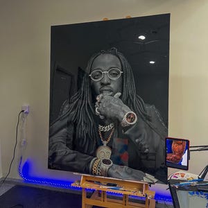 Puede incluir: Una pintura de retrato en blanco y negro de un hombre con rastas largas que lleva una chaqueta negra, una cadena de oro y un reloj de oro. La pintura está en un caballete de madera en una habitación con luces LED azules.