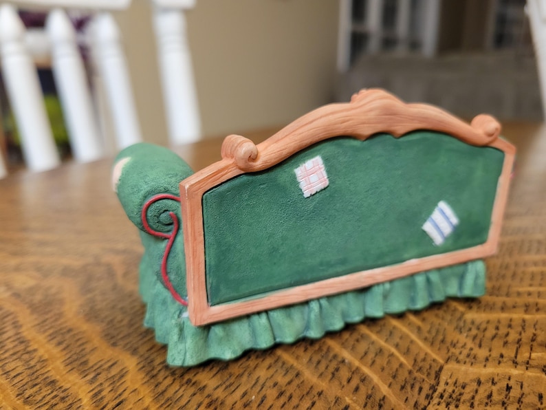 K&ouml;nnte beinhalten: Ein gr&uuml;nes Miniatursofa mit Holzrahmen und gr&uuml;nem Kissen. Das Sofa hat einen ger&uuml;schten Rock und dekorative Aufn&auml;her auf der R&uuml;ckseite. Das Sofa ist ein dekorativer Gegenstand.