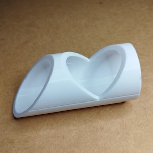 以下が含まれることがあります： 白くてハート型の装飾品。このオブジェクトは、中央にハートの切り抜きがある、曲がったチューブ状の構造です。このオブジェクトは、滑らかでしっかりとした素材で作られています。