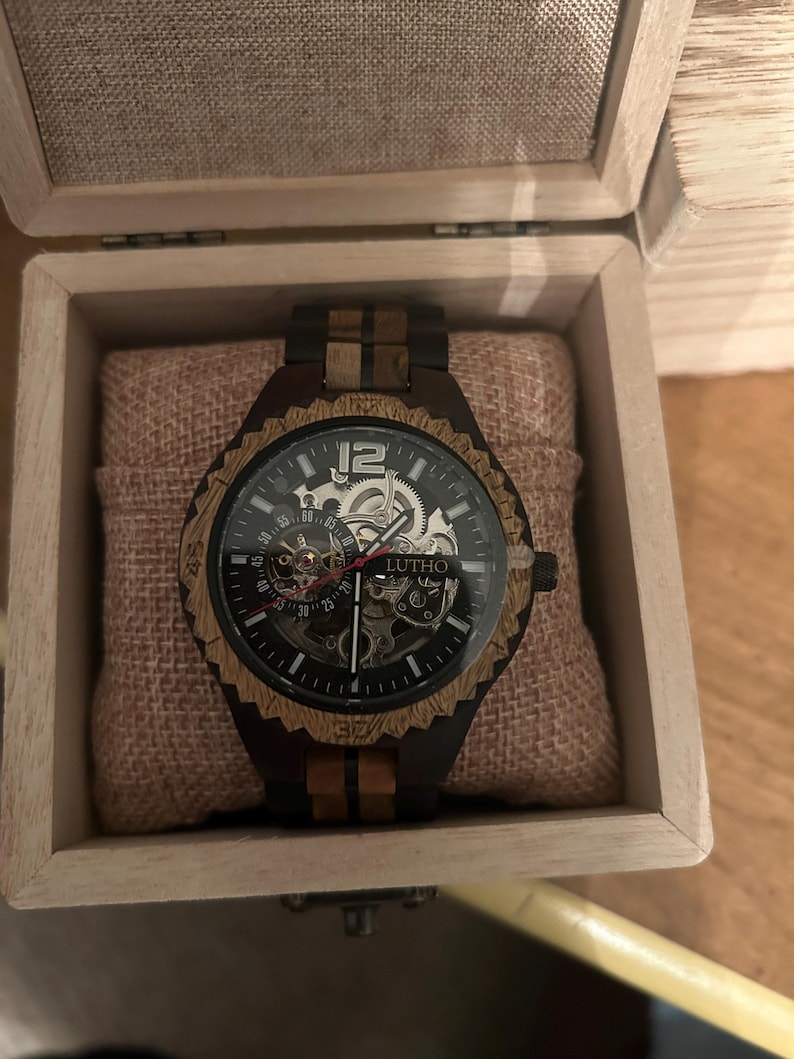 May include: A wooden wristwatch with a black face and visible gears, presented in a wooden box. The watch features a brown and black wooden bezel and band. The watch face displays the brand name "LUTHO".