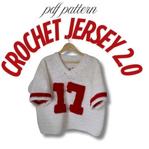 May include: A white crochet jersey with red accents and the number 17 on the front. The jersey has a V-neck and short sleeves with red stripes. The words "CROCHET JERSEY 2.0" are in red above the jersey.