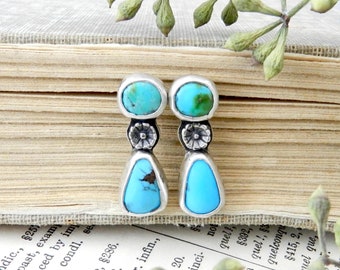 May include: A pair of silver dangle earrings with turquoise stones. The earrings feature a small flower design and a teardrop-shaped turquoise stone.