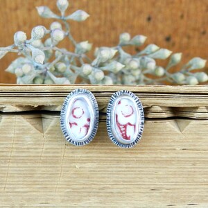 May include: A pair of oval-shaped earrings with a silver setting and a red and white patterned design.