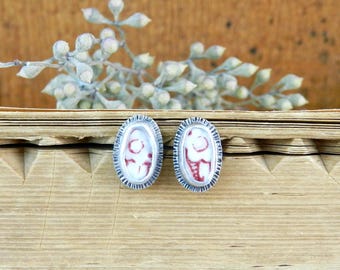 May include: A pair of oval-shaped earrings with a silver setting and a red and white patterned design.