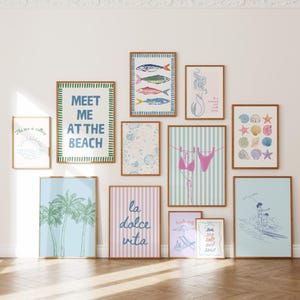 May include: A gallery wall set of eleven framed prints featuring coastal themes, including palm trees, seashells, a mermaid, a bikini on a clothesline, and text art reading "MEET ME AT THE BEACH" and "la dolce vita" in various colors and styles.