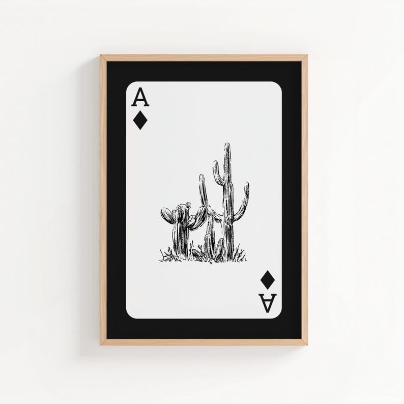 May include: Framed art print featuring a playing card design. The Ace of Diamonds card displays a black and white illustration of two cacti. The card is set against a white background, framed in black and a natural wood tone.
