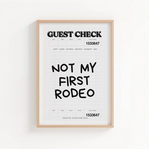 May include: Framed print featuring a mock guest check design. The top reads "GUEST CHECK" and includes a check number. The phrase "NOT MY FIRST RODEO" is prominently displayed in bold, black letters. The print is in a light wood frame.